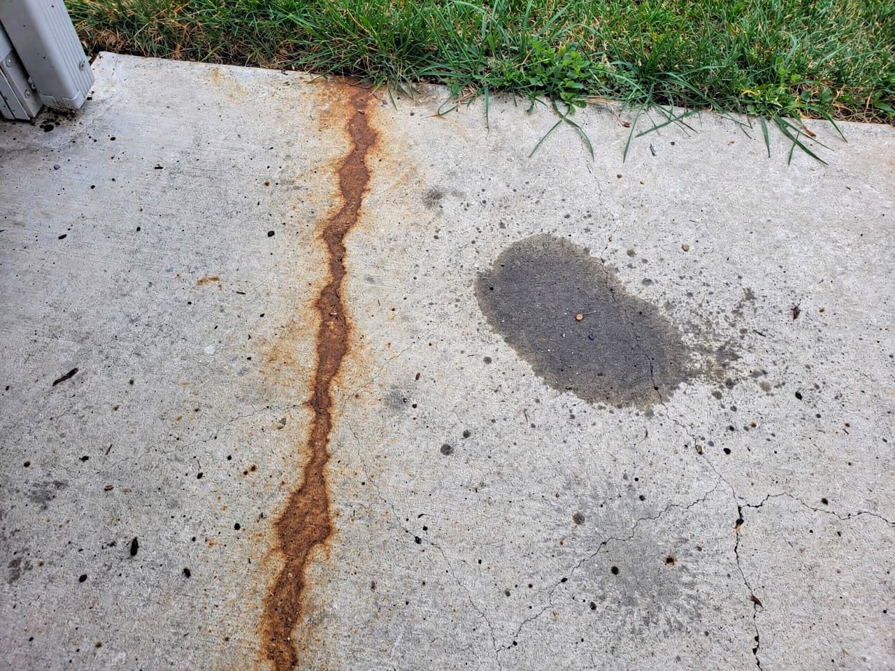 A rust streak and oil spot staining a concrete slab before treatment